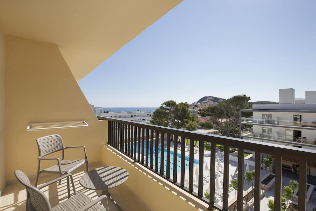Un balcon avec deux chaises et une table, donnant sur une piscine et des immeubles.