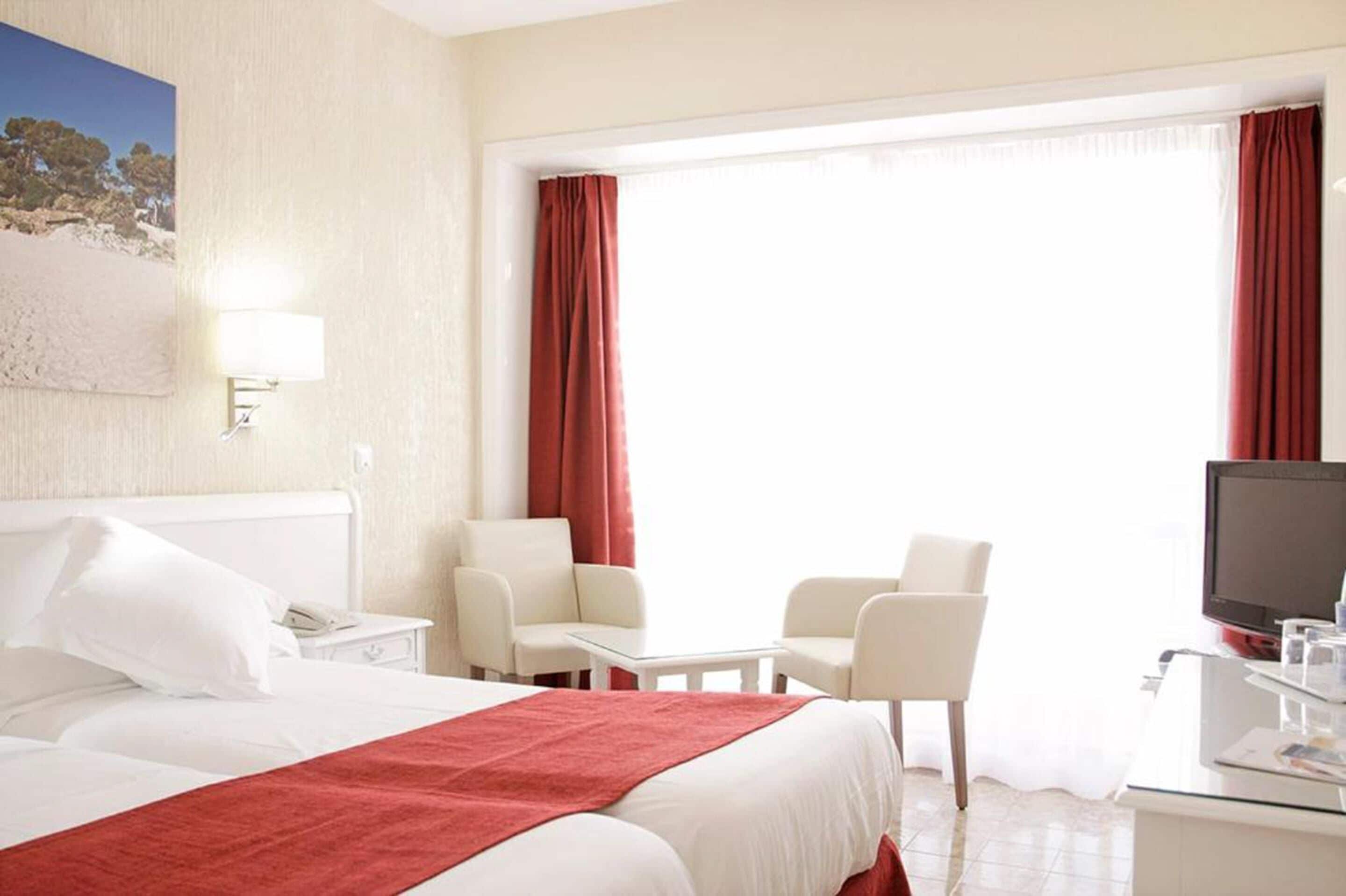 Habitación de hotel con cama, escritorio, silla, televisión y ventana con cortinas.