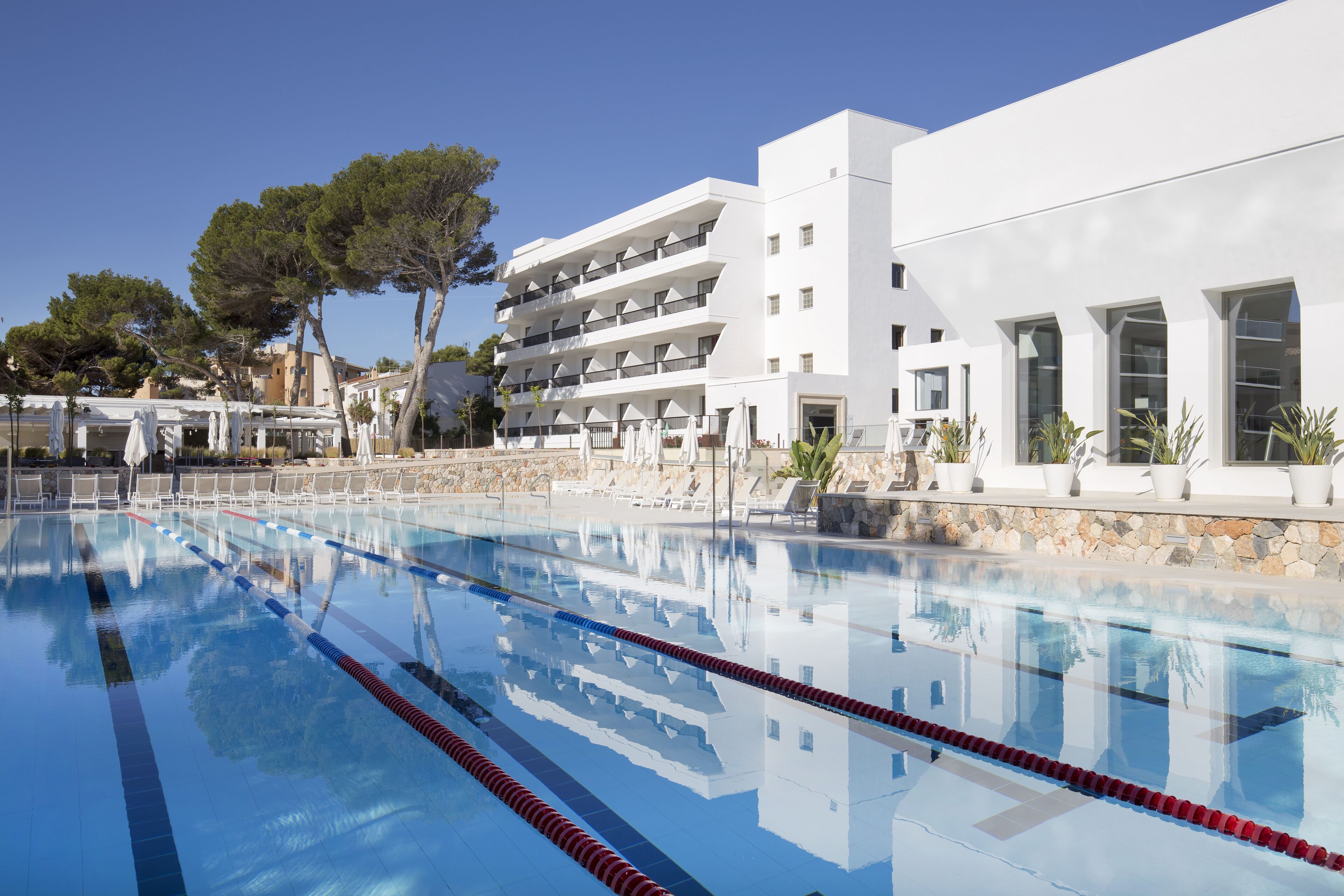 A swimming pool with clear blue water, surrounded by white buildings and trees.