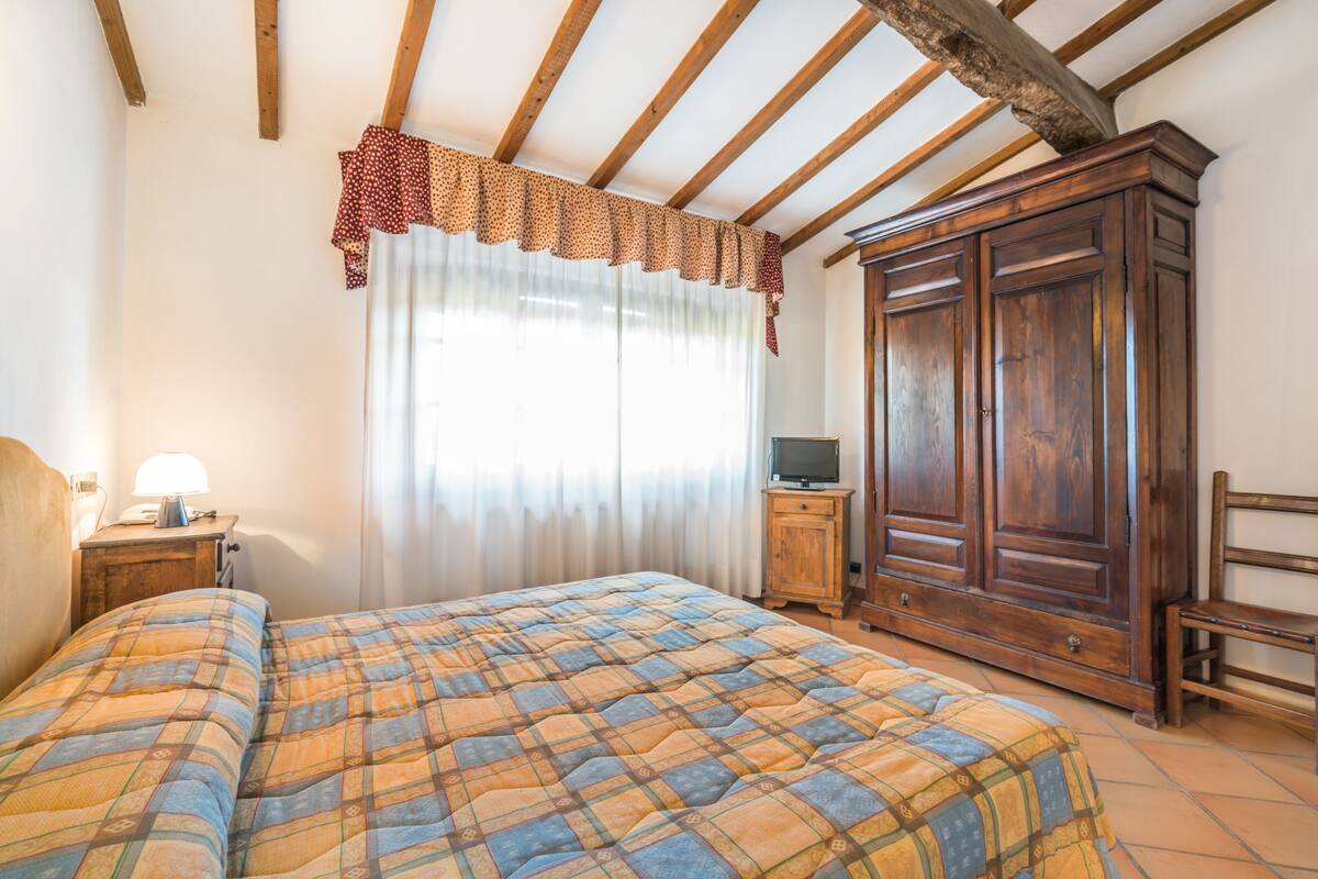 A bedroom with a bed, wooden wardrobe, and a television on a wooden cabinet.