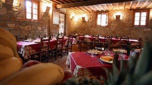 Un comedor rústico con paredes de piedra y vigas de madera, con varias mesas dispuestas para comer y sillas.