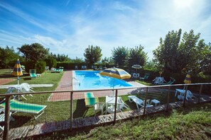 A swimming pool with lounge chairs and umbrellas, surrounded by a fence and greenery. - Agriturismo Palazzo Bandino (Chianciano Terme)