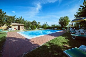 A rectangular swimming pool with a brick border, surrounded by grass and trees. - Agriturismo Palazzo Bandino (Chianciano Terme)