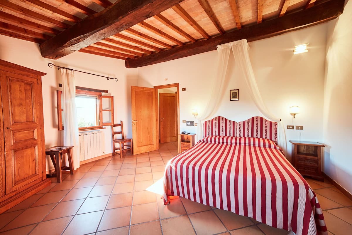 A bedroom with a wooden ceiling, a bed with a striped bedspread, a chair, a wooden cabinet, and a window with curtains.