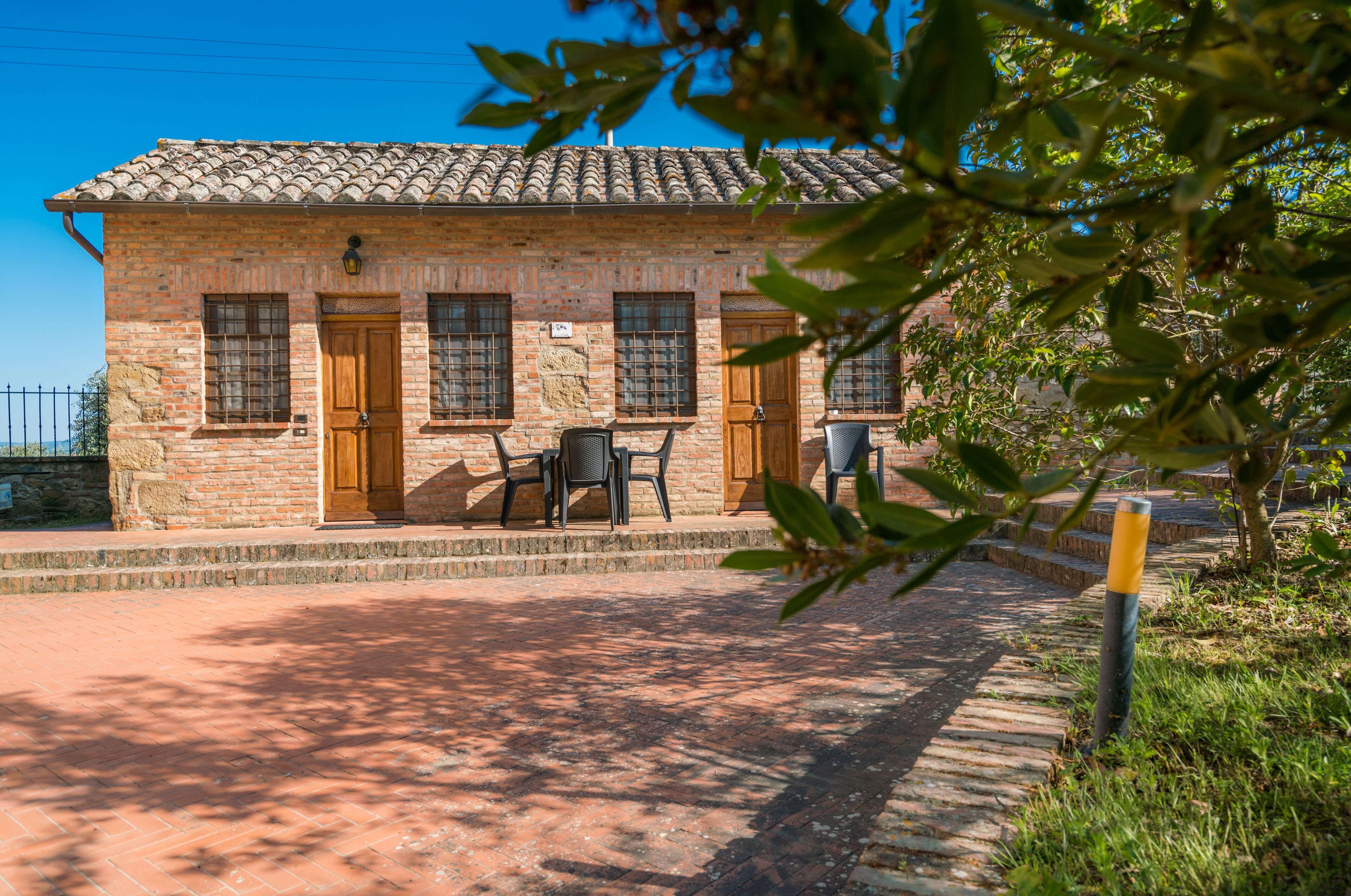 A stone building with a tiled roof, two wooden doors, and a small outdoor seating area with two chairs.