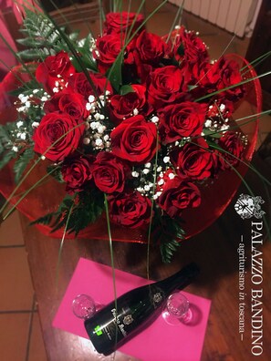 A bouquet of red roses in a red vase with a bottle of wine and glasses on a pink table. - Agriturismo Palazzo Bandino (Chianciano Terme)