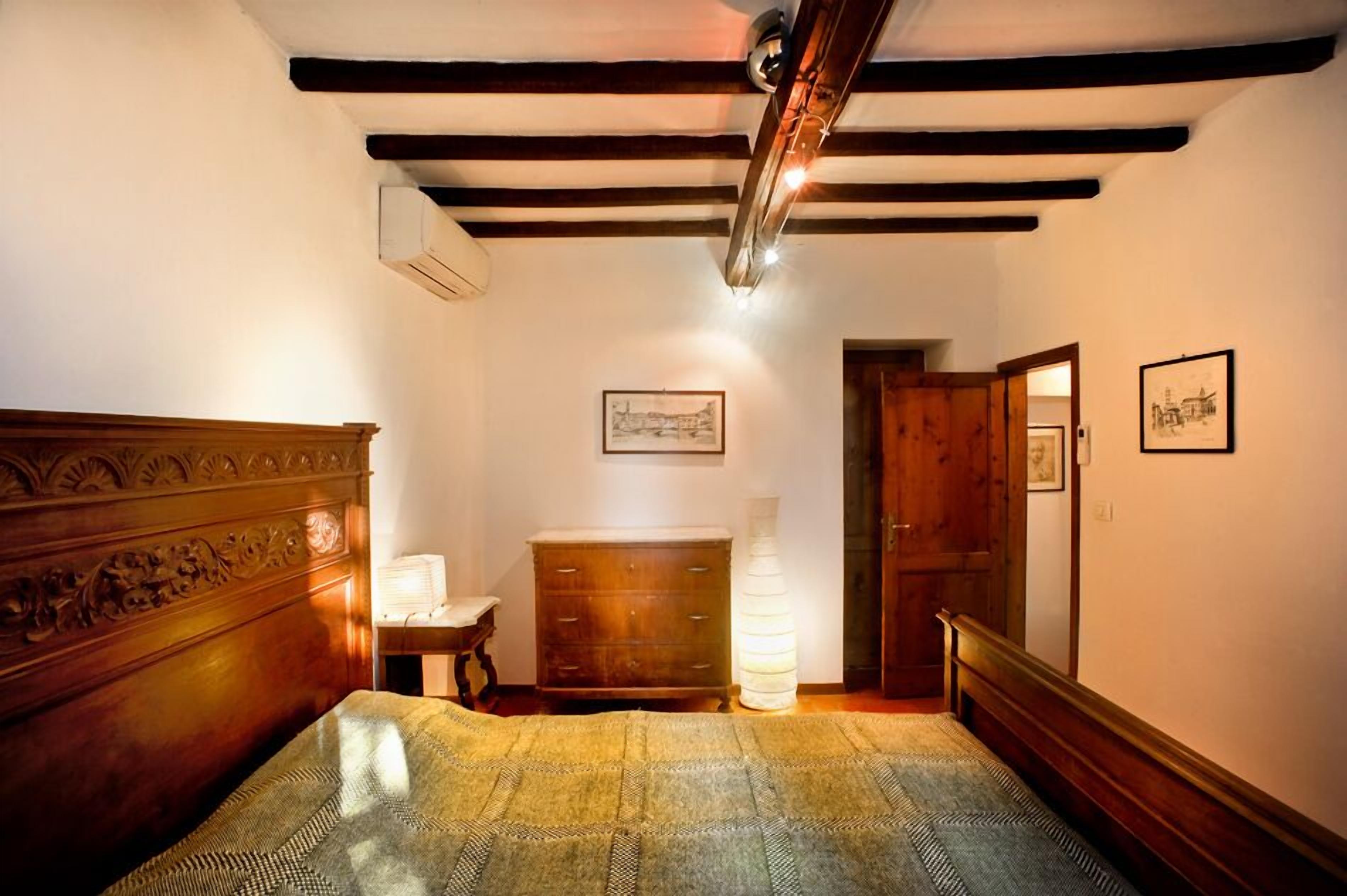 A bedroom with a wooden bed, a dresser, a nightstand, and a wall-mounted lamp.