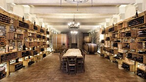 A wine cellar with wooden shelves and barrels, a long table, and a chandelier. - Relais La Torre (Arezzo)