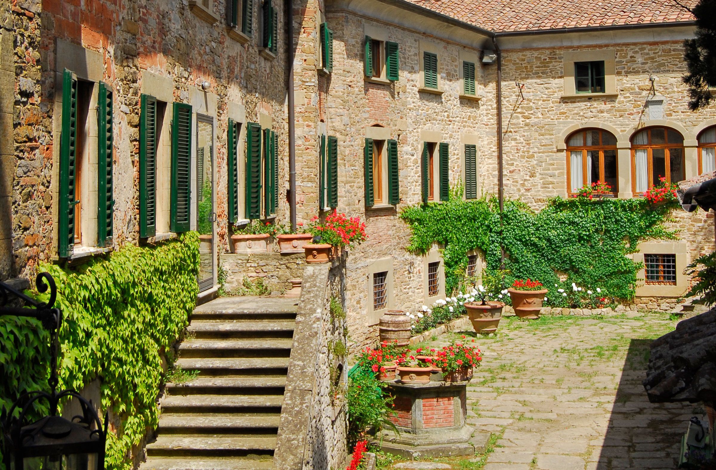 Ein Steinhaus mit grünen Fensterläden, einem Innenhof mit Stufen und Topfpflanzen.