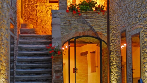 A stone building with a staircase leading to an entrance, a balcony with flowers, and a door with glass panels. - Relais La Torre (Arezzo)