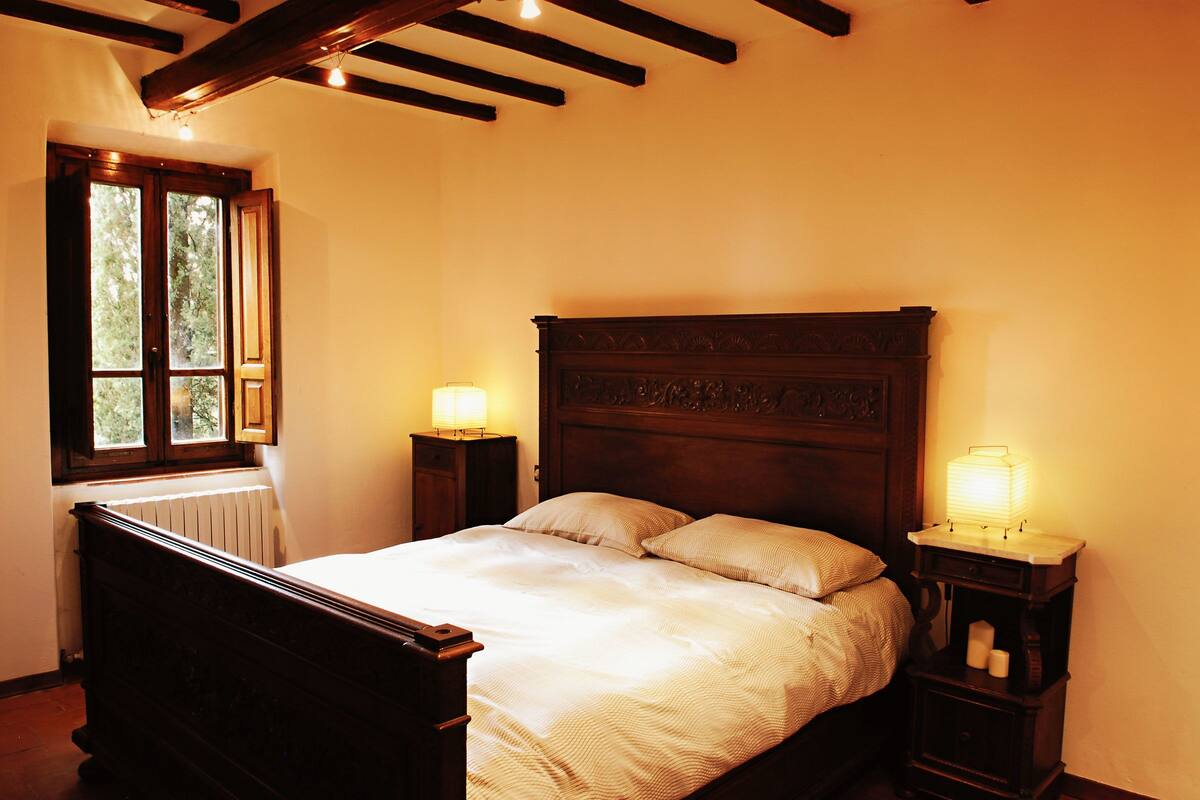 A bedroom with a wooden bed, two bedside tables with lamps, a window, and a radiator.