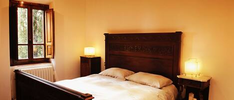A bedroom with a wooden bed, two bedside tables with lamps, a window, and a radiator.