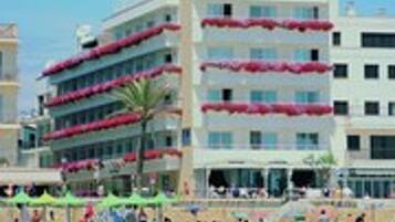 A hotel with multiple balconies, a beach in the background, and a clear sky.
