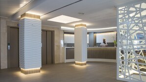 A modern reception area with a receptionist, wooden pillars, and a decorative partition. - Hotel Voramar Mallorca (Son Servera)