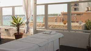 A room with a massage table, a potted plant, and a view of the sea through large windows. - Hotel Voramar Mallorca (Son Servera)