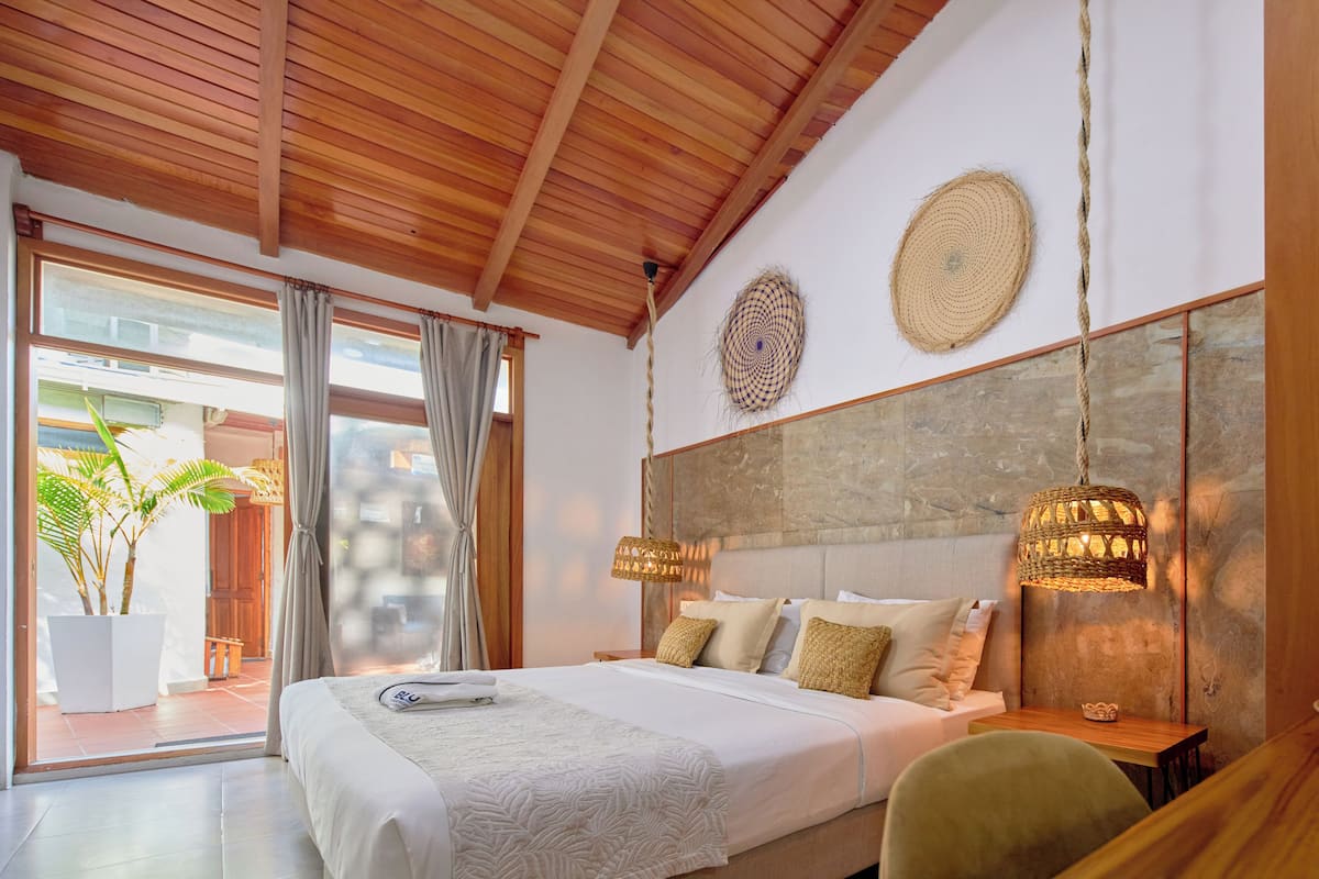 A modern bedroom with a large bed, two hanging lamps, and a view of the outdoors.