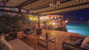 An outdoor patio with wooden flooring, wicker furniture, and a view of the ocean at night.