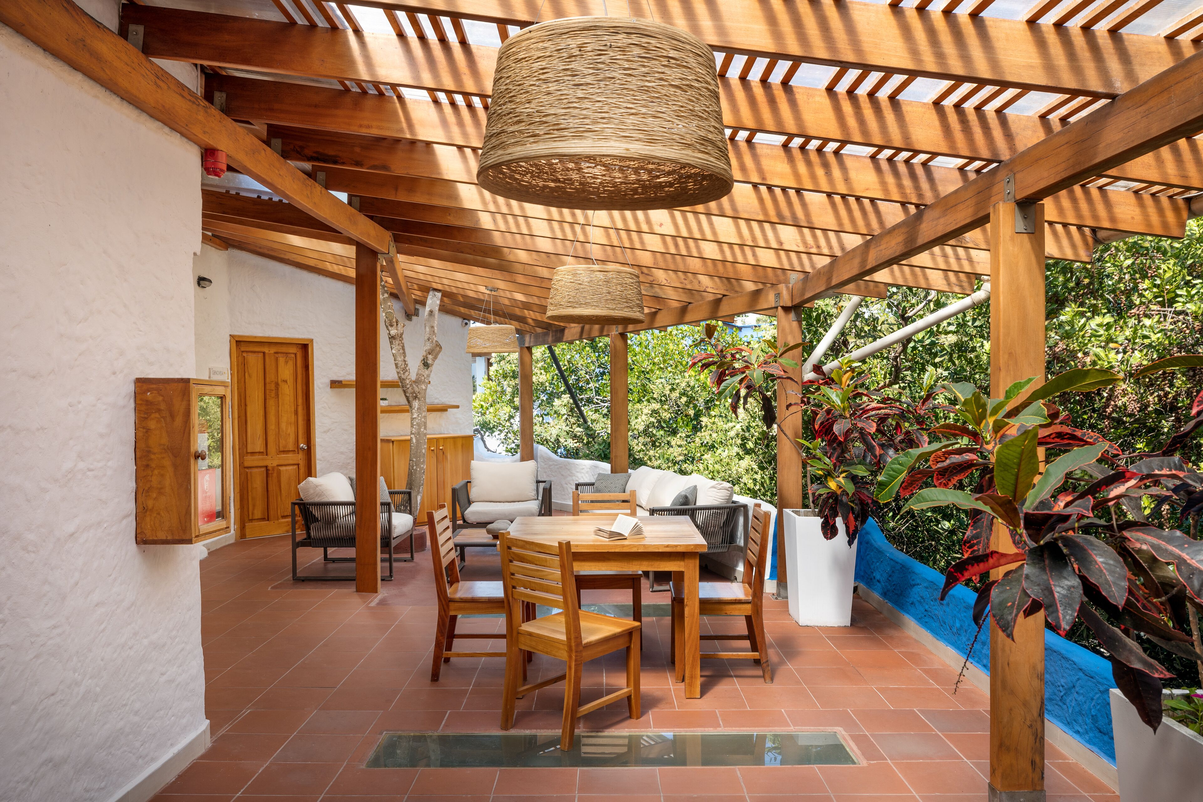A covered patio area with a wooden table and chairs, a sofa, and a hanging light fixture.