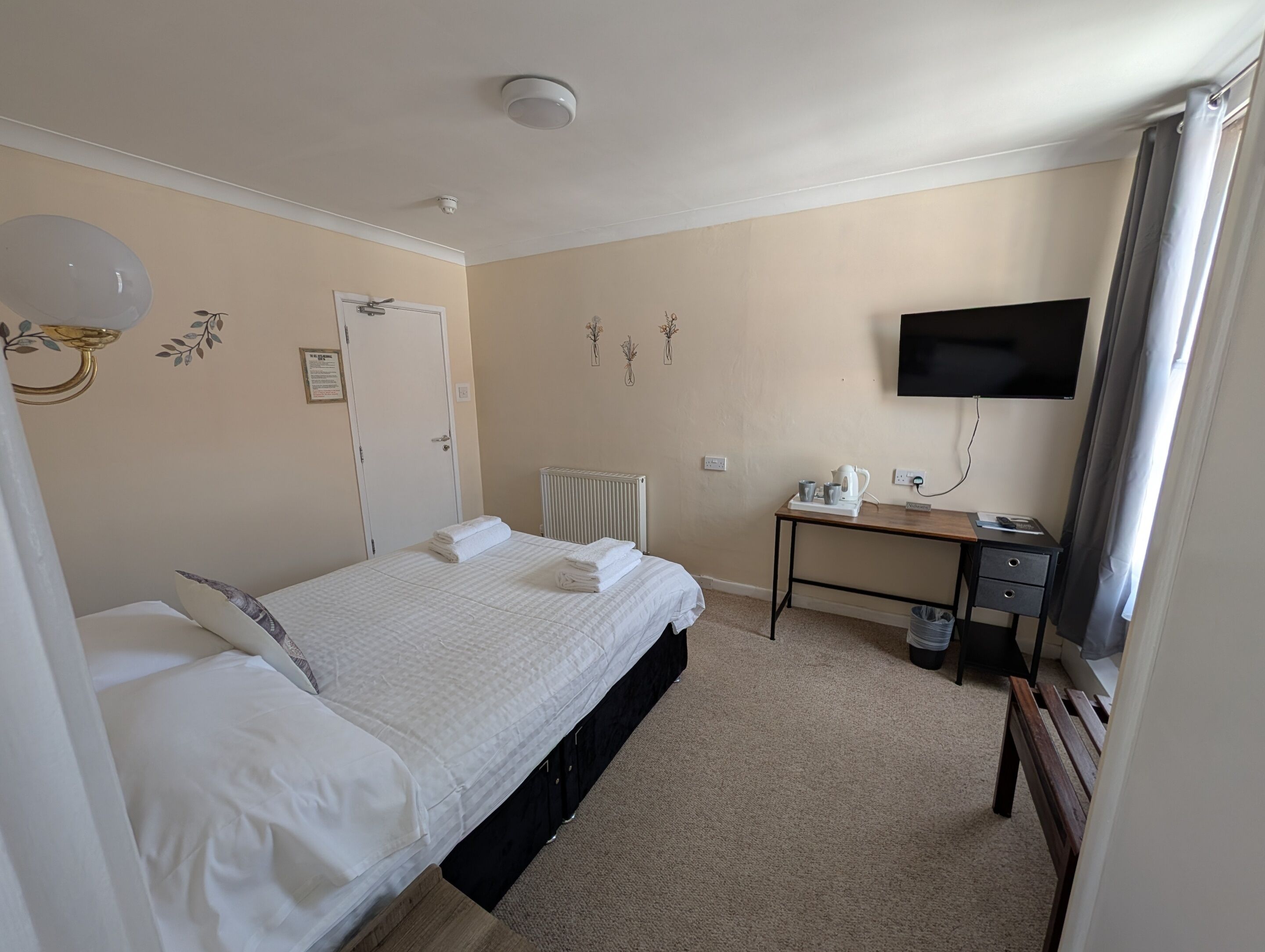 Une chambre d’hôtel équipée d’un lit, d’un bureau, d’un radiateur, d’une télévision et d’un luminaire fixé au mur.