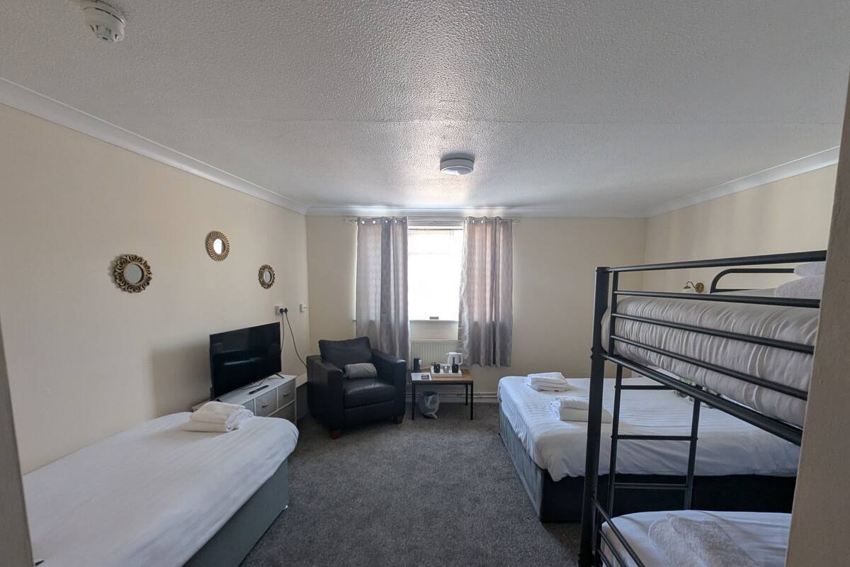 A hotel room with bunk beds, a flat-screen TV, a chair, a small table, and a window with curtains.