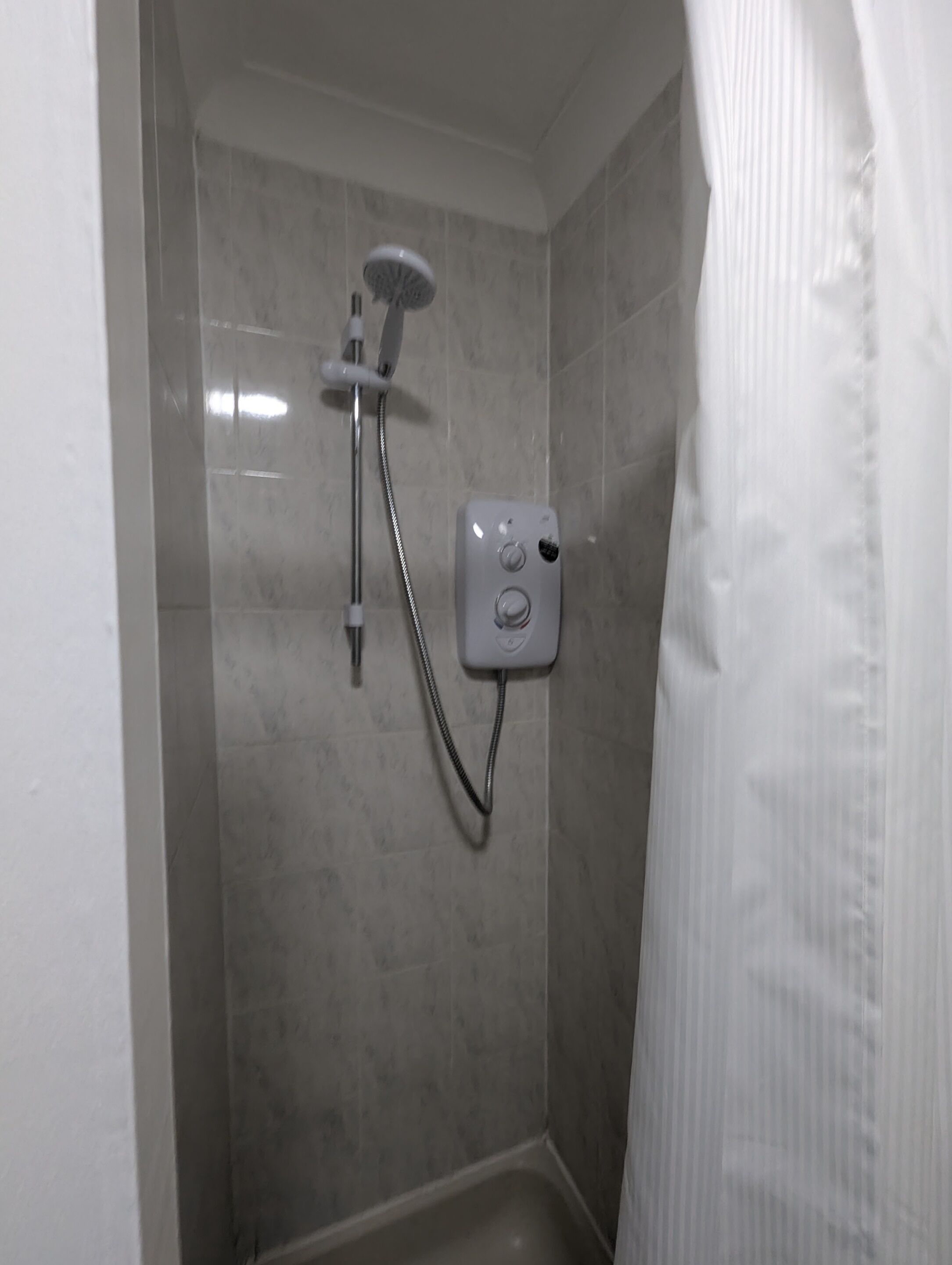 Een douche met een handdouche, een bedieningspaneel aan de muur en een betegelde vloer.