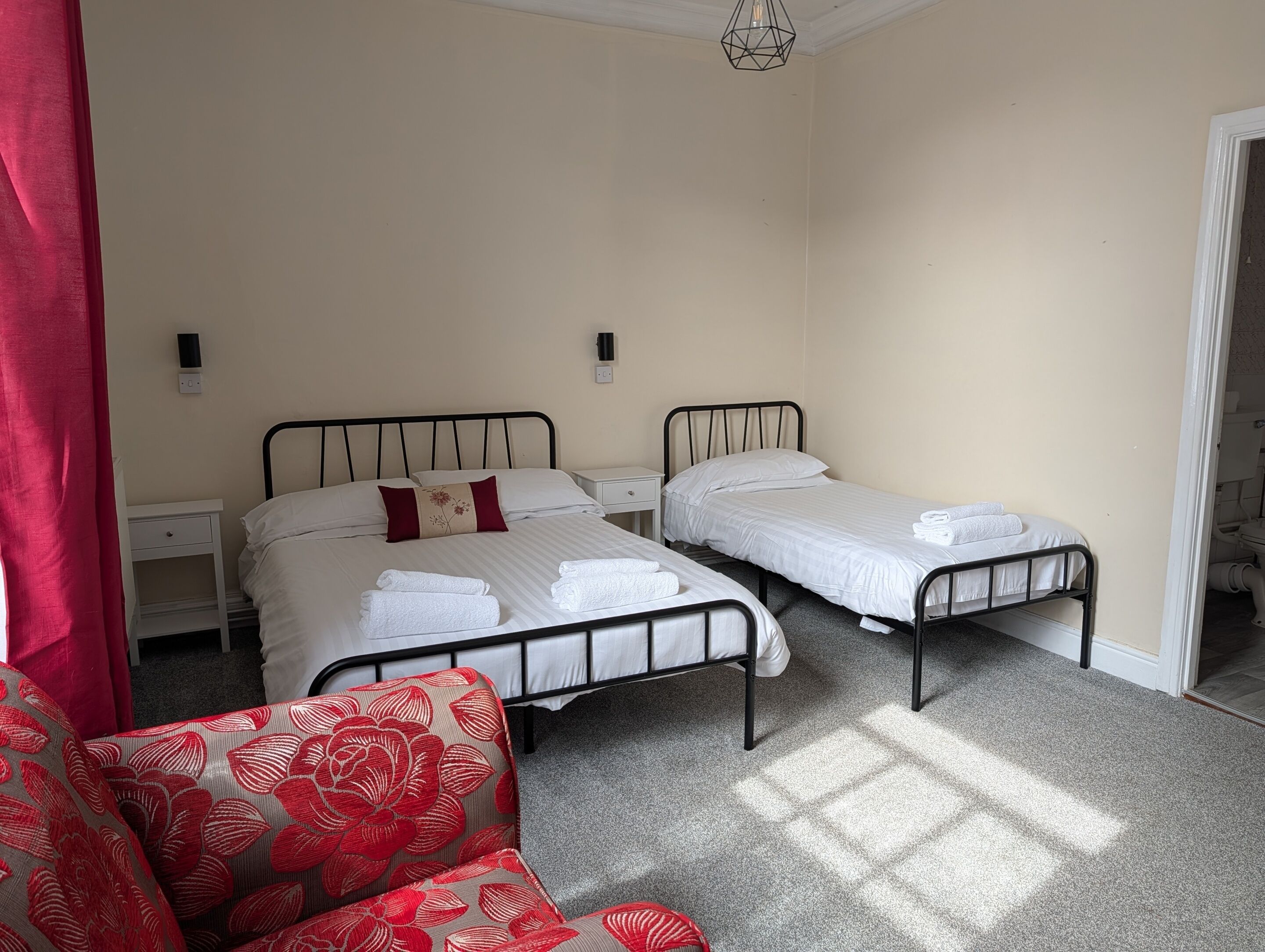 A bedroom with two single beds, a nightstand, a chair, and a door leading to another room.