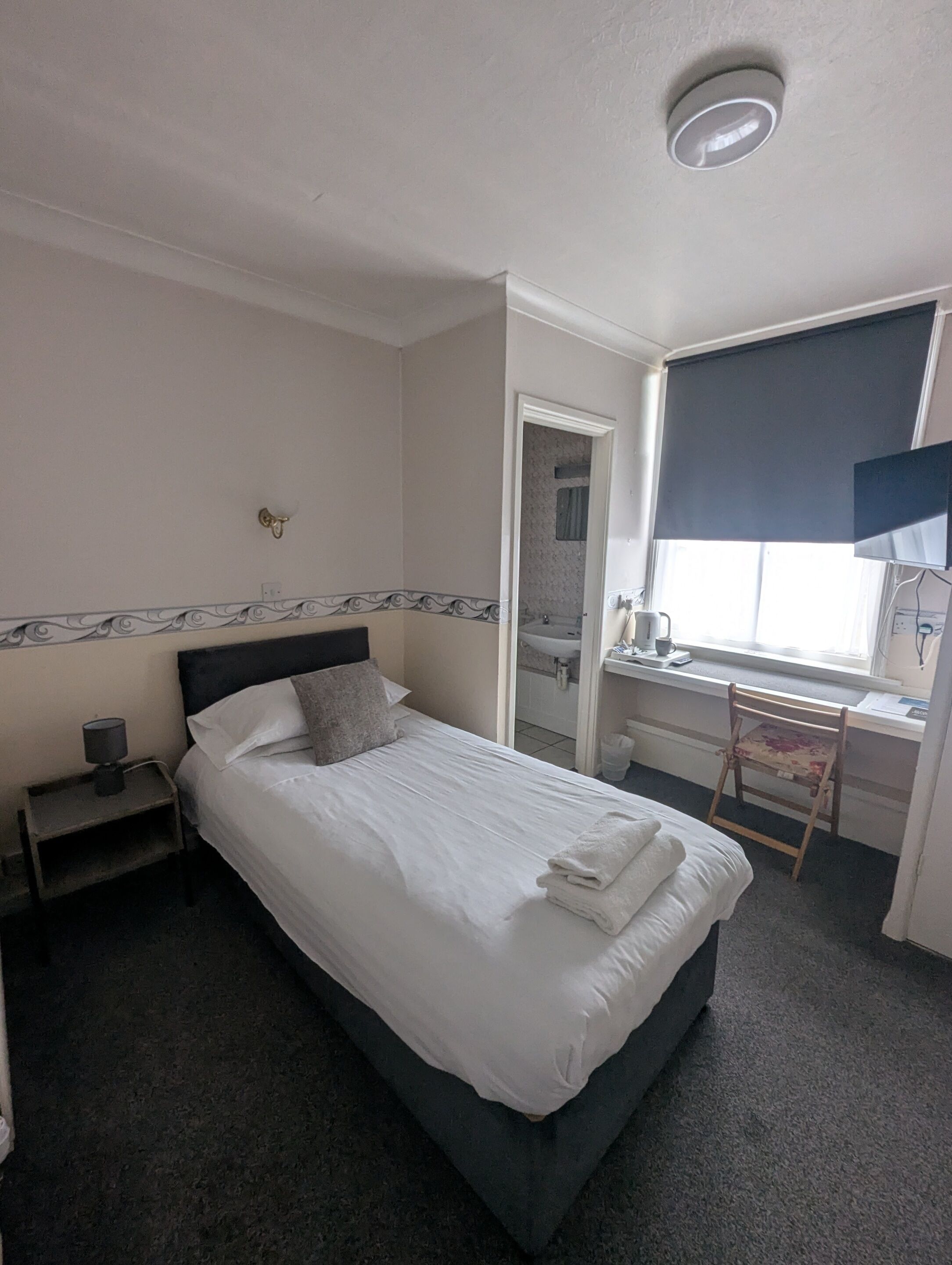 Una habitación de hotel con cama, escritorio, silla, ventana y espejo.