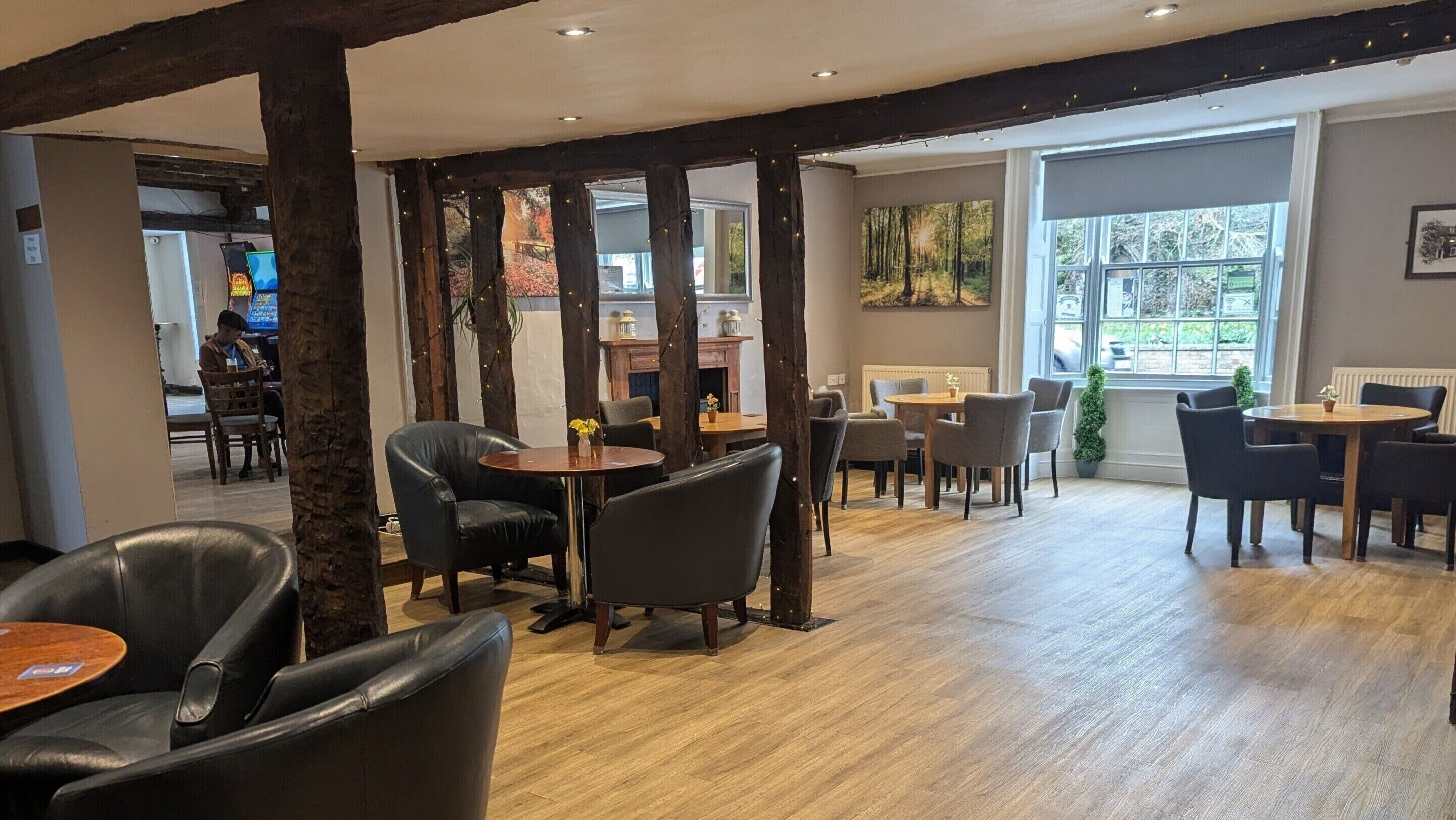 A spacious indoor area with wooden beams, multiple seating arrangements, and large windows providing natural light.