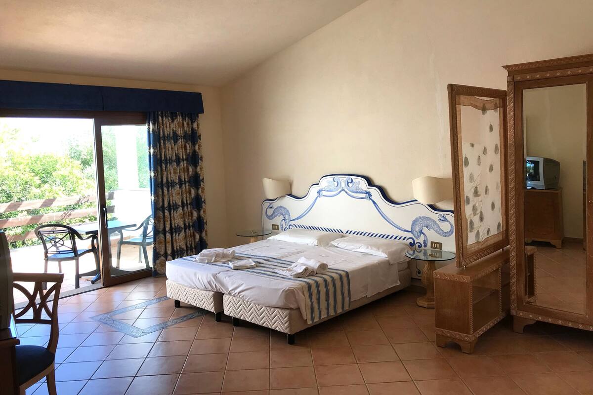 A hotel room with a bed, a mirror, a television, and a view of the outdoors.