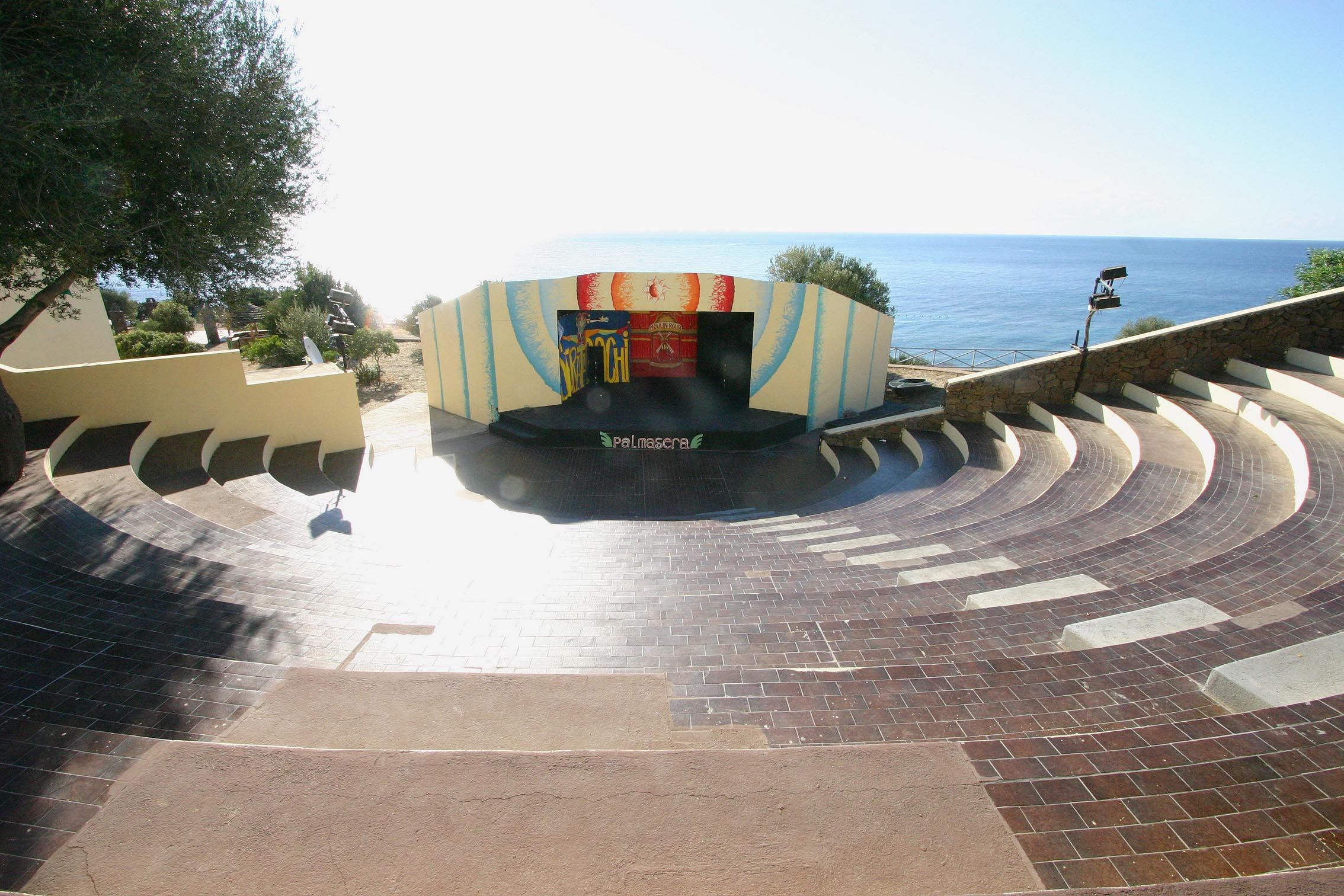 A curved brick pathway leading to a building with a colorful facade and a view of the sea.