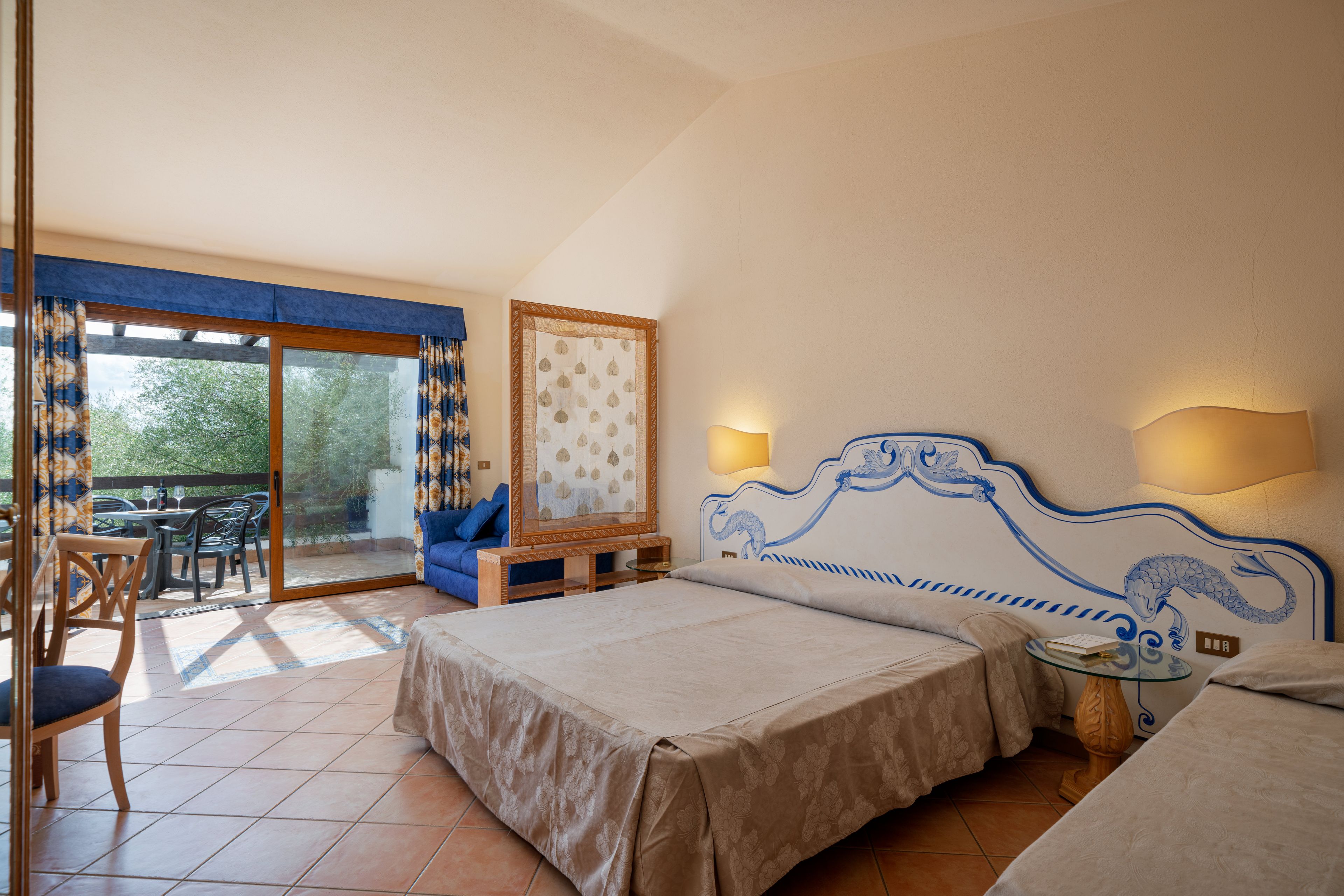 A bedroom with a bed, a sofa, a table, and a view through a glass door.