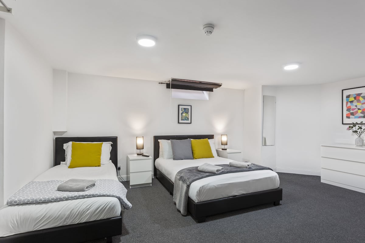 Quarto de hotel moderno com duas camas de solteiro, uma janela grande e uma televisão de tela plana.