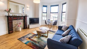A modern living room with a blue sofa, a fireplace, a TV, and a dining area with chairs and a table. - River Rooms Nottingham (Nottingham)