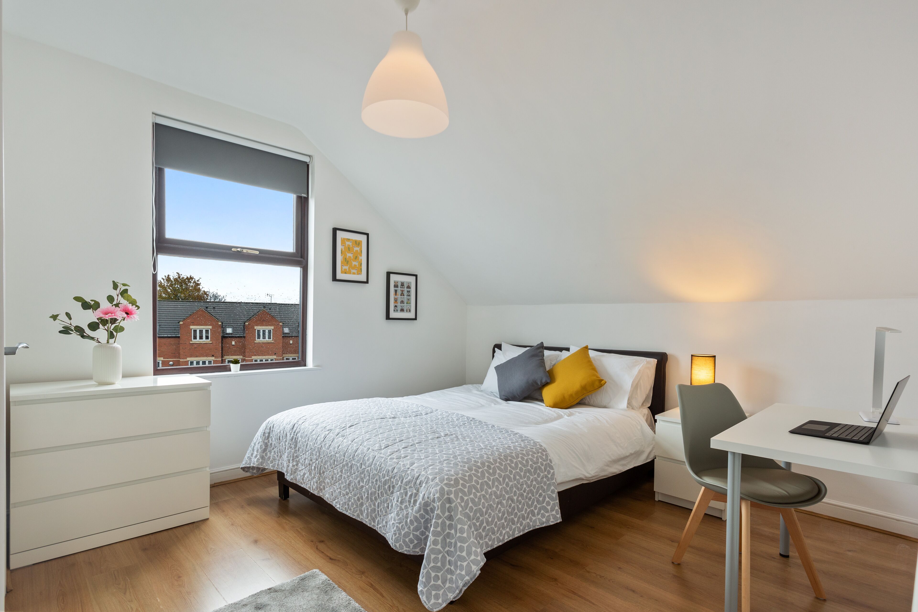 A modern bedroom with a bed, bedside table, desk, and a large window.