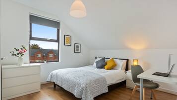 Een moderne slaapkamer met een bed, nachtkastje, bureau en een groot raam.