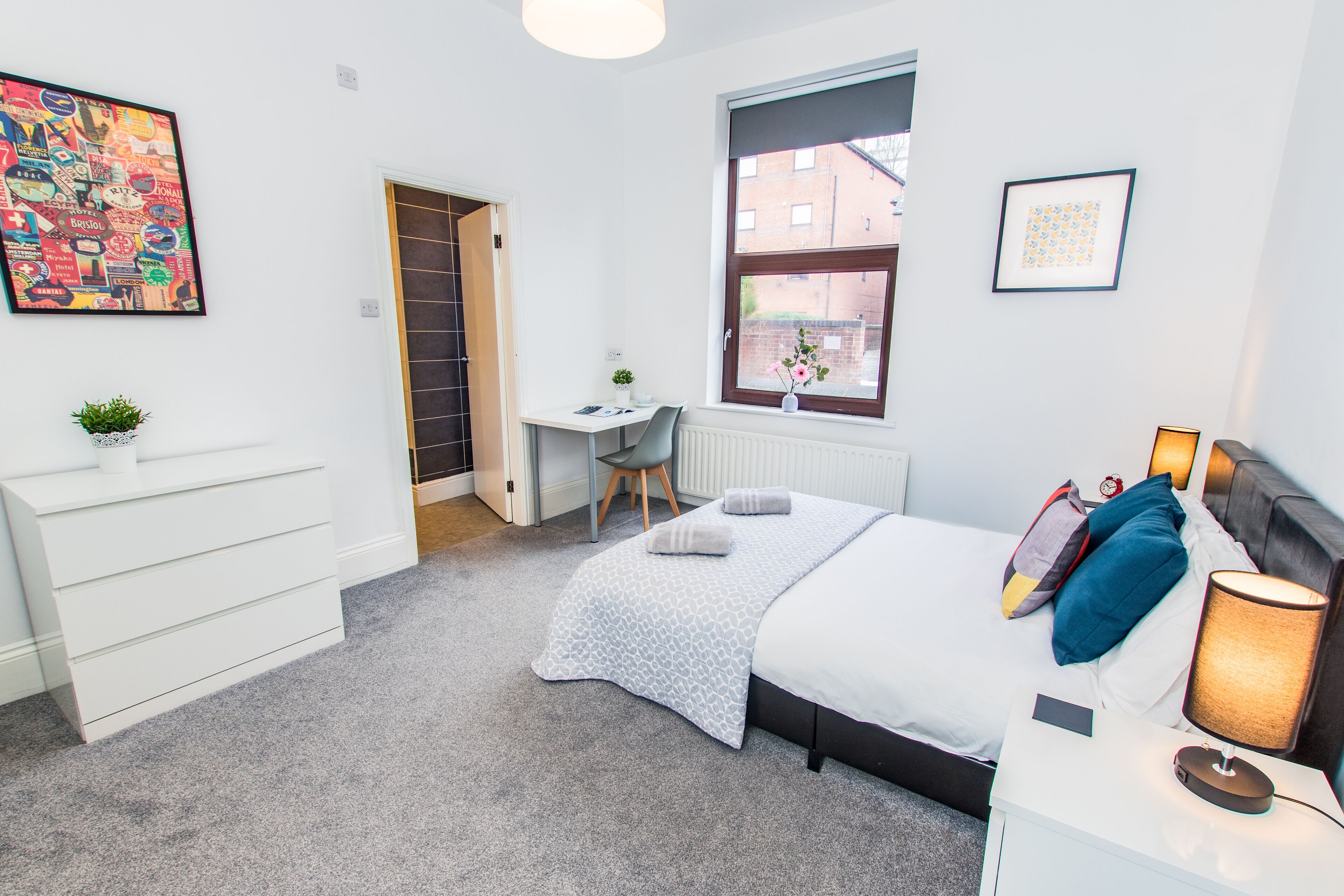 A bedroom with a bed, bedside table, lamp, desk, chair, and a radiator.