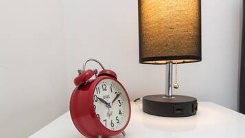 A red alarm clock with a white face and black numbers, placed on a white surface next to a lamp with a textured shade.