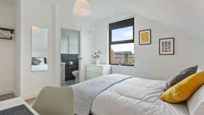 A modern bedroom with a bed, a desk, and a window with a view of buildings. - River Rooms Nottingham (Nottingham)