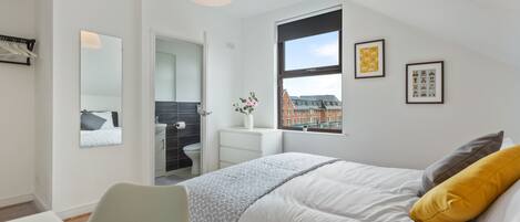 A modern bedroom with a bed, a desk, and a window with a view of buildings.