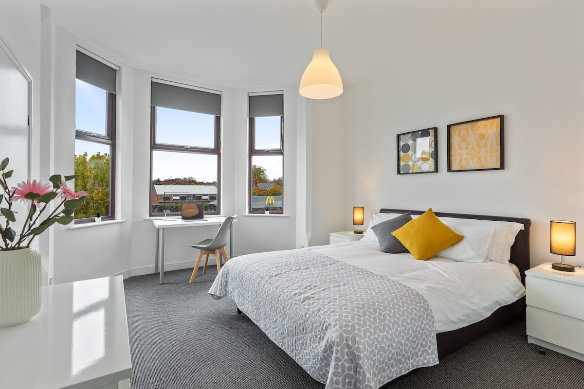 Quarto de hotel moderno com uma cama grande, uma escrivaninha e vista para a água através de amplas janelas.