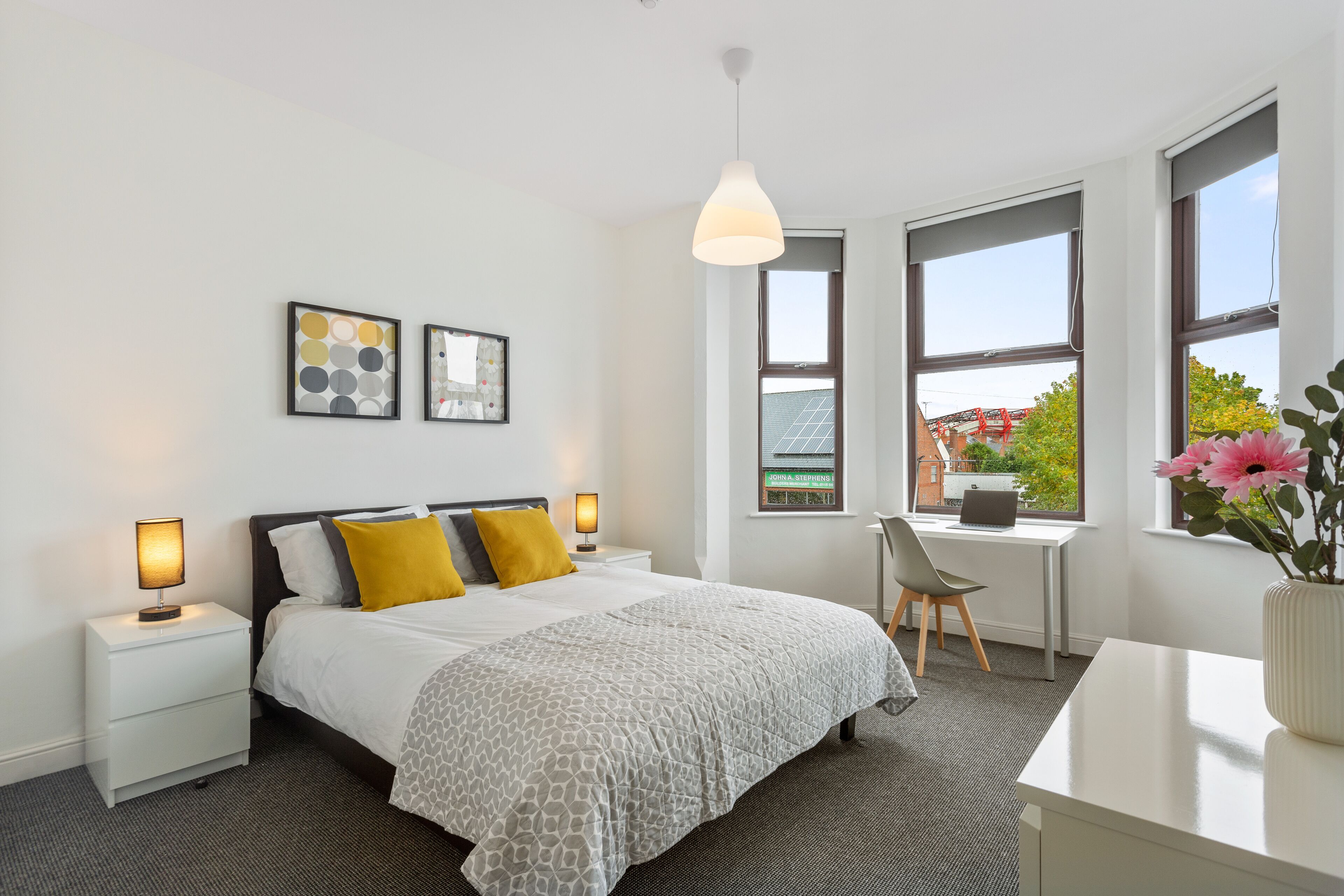 A modern hotel room with a bed, bedside lamps, a desk, and a view of a building outside.