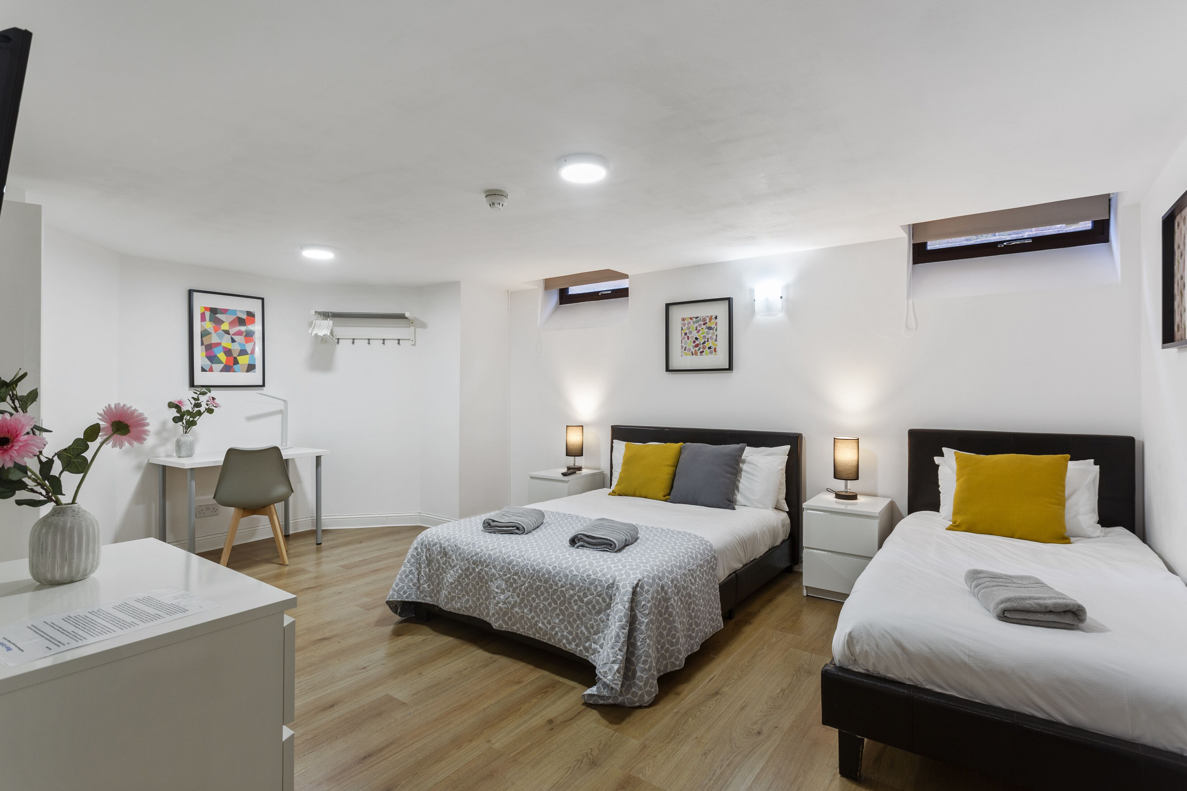 A modern hotel room with two beds, a desk, and a chair.