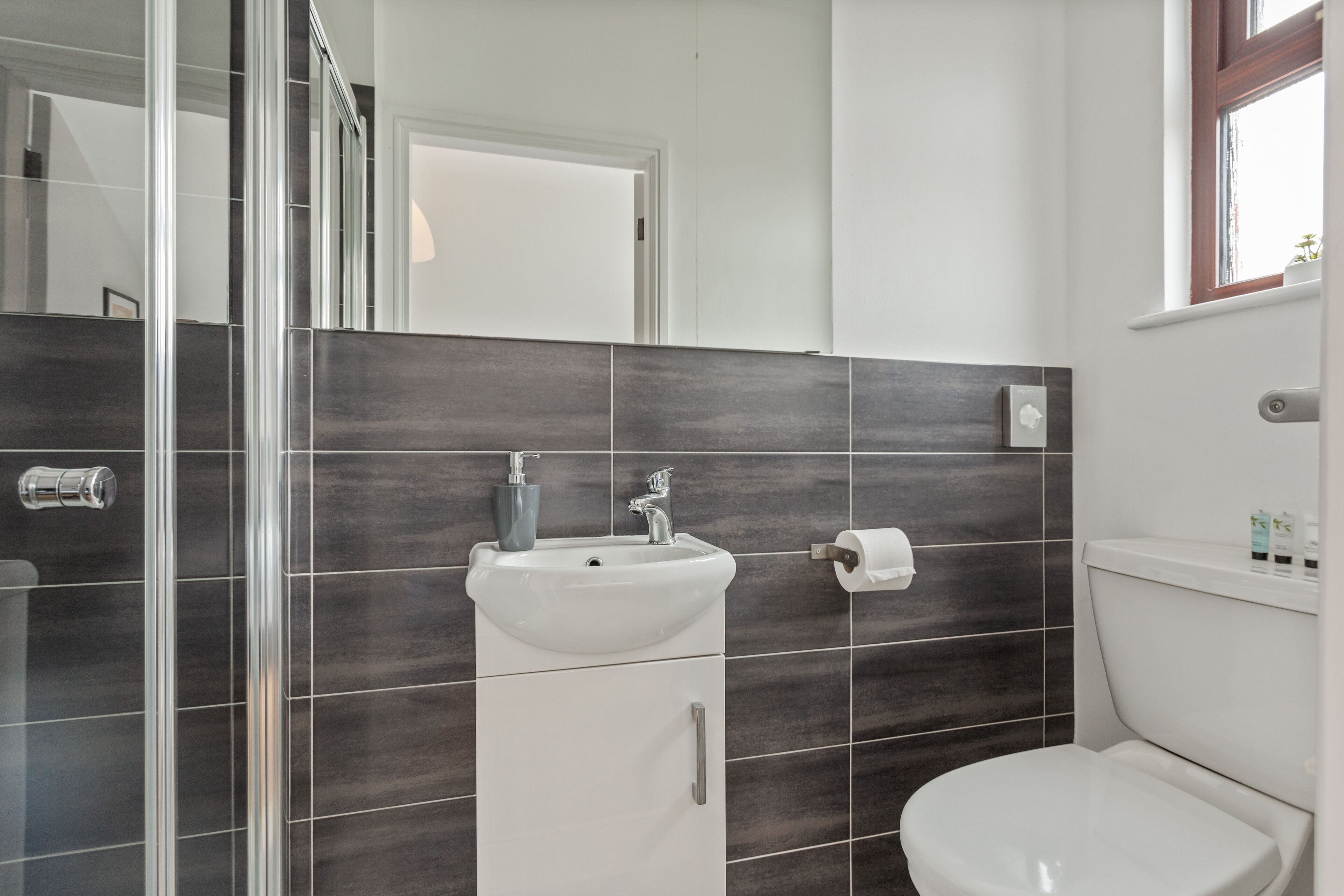 A modern bathroom with a glass shower enclosure, a white sink with a faucet, and a toilet.