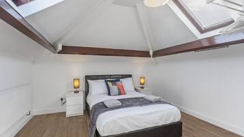 A bedroom with a skylight, a bed with a dark headboard, white nightstands, and a white radiator.
