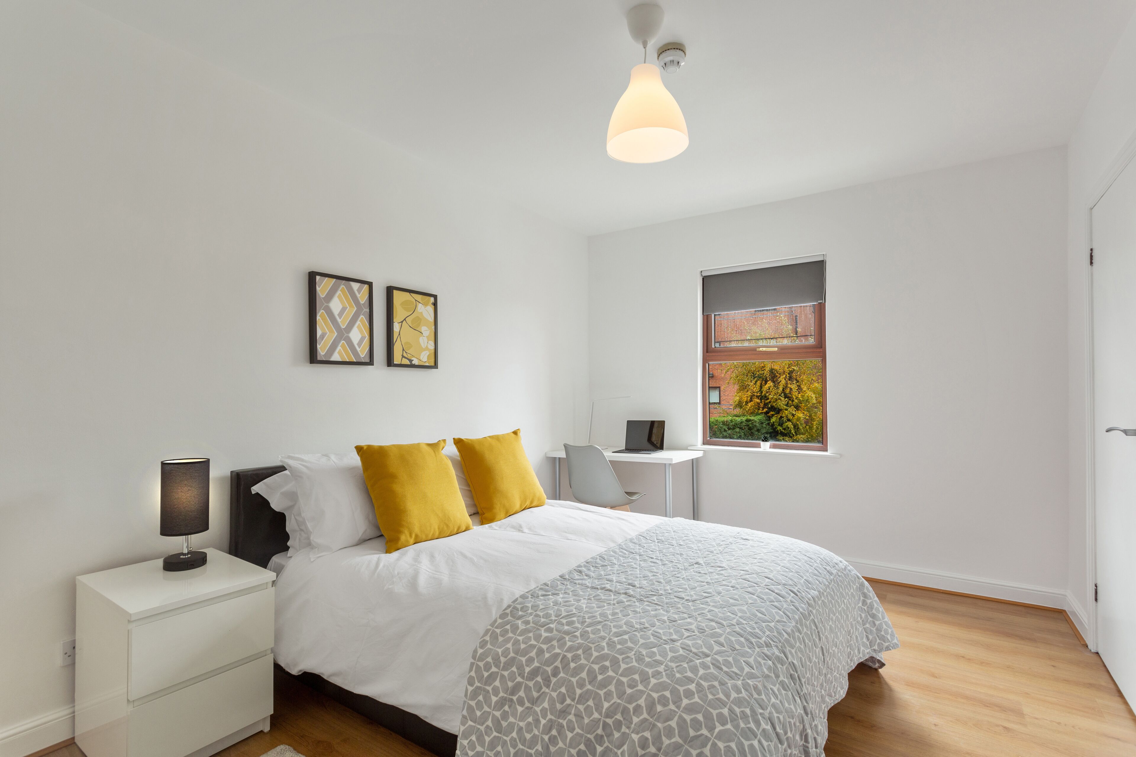 A modern bedroom with a bed, bedside tables, a desk, and a window with a view of greenery.