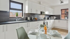 A modern kitchen with white cabinets, a black countertop, and a dining area with a table set for four. - River Rooms Nottingham (Nottingham)