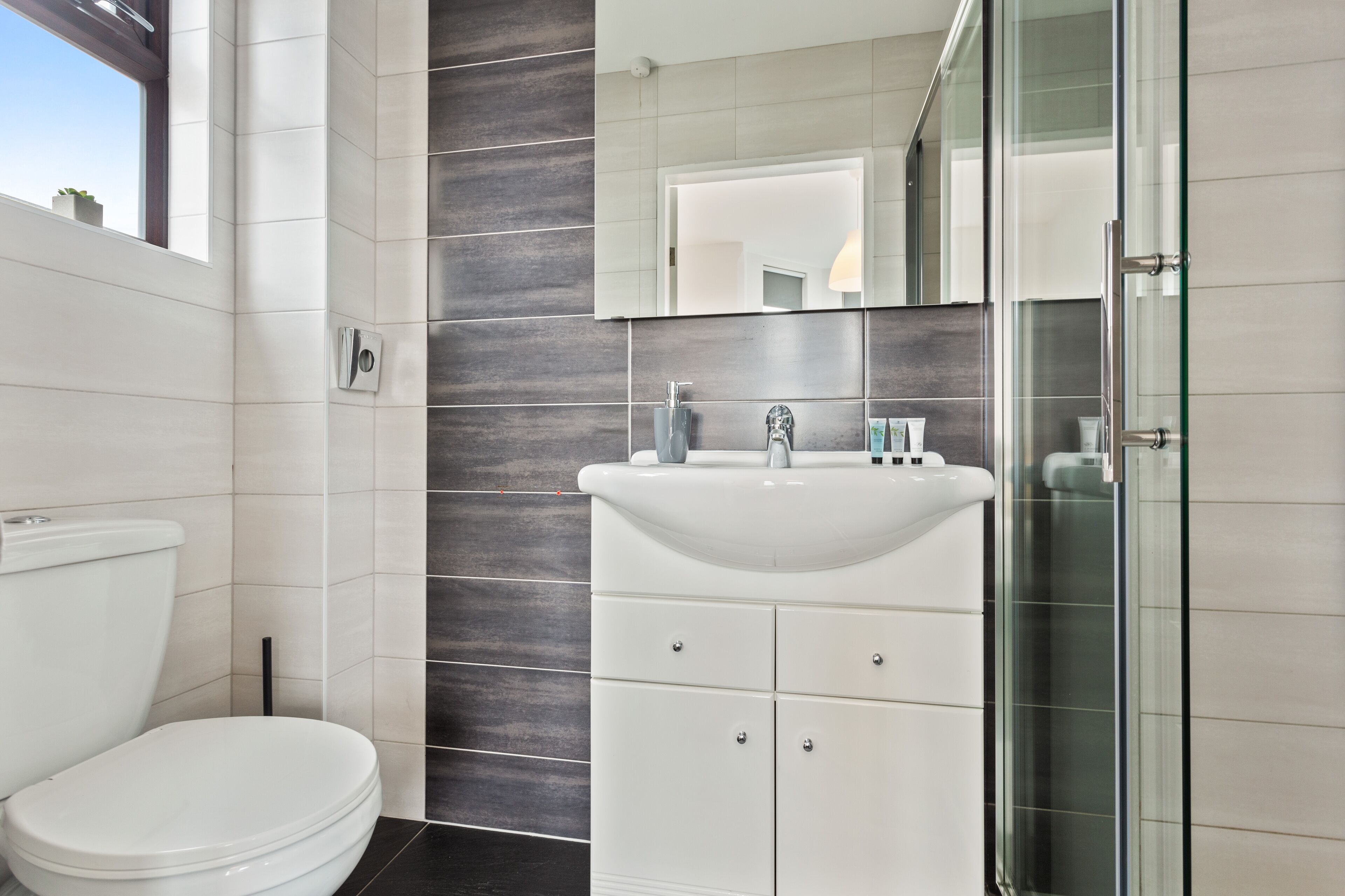 Une salle de bain moderne comprenant des toilettes, un lavabo avec un miroir au-dessus et un espace douche.