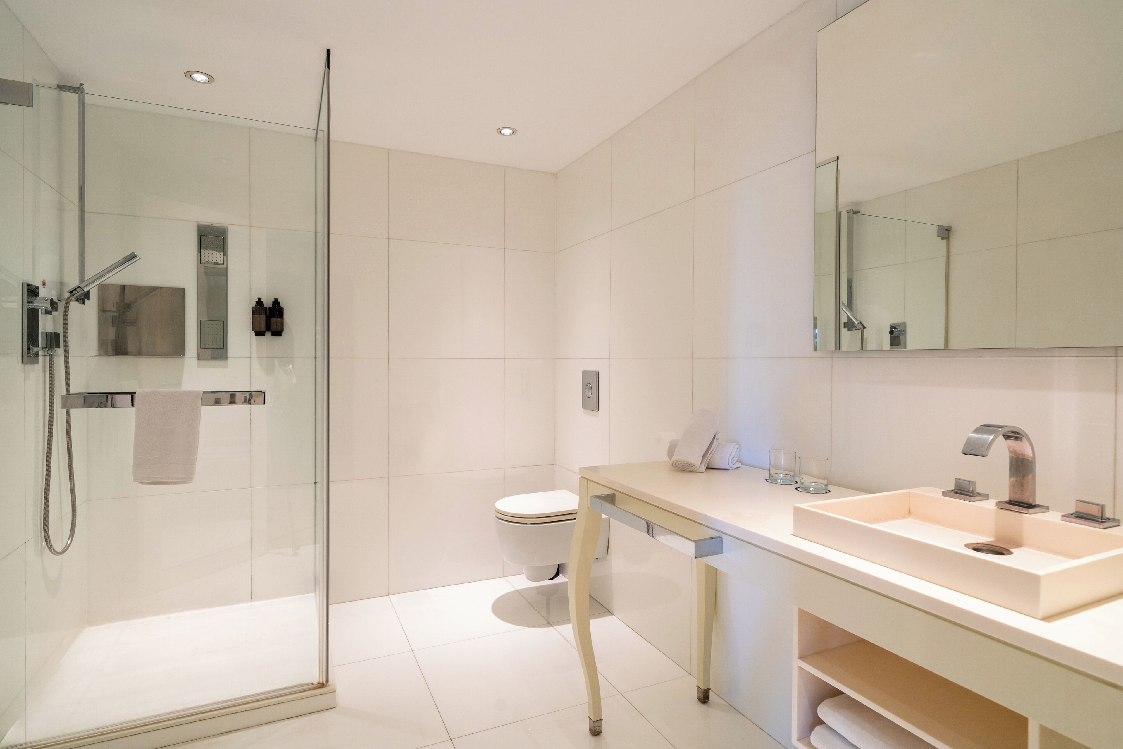 Un baño moderno con ducha envuelta en vidrio, un lavamanos blanco y un espejo grande.