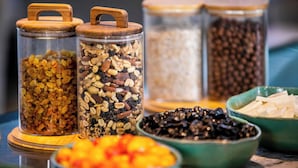 Drei Gläser mit Holzböden, gefüllt mit verschiedenen Nüssen und Trockenfrüchten, und eine Schüssel geschnittener Äpfel.