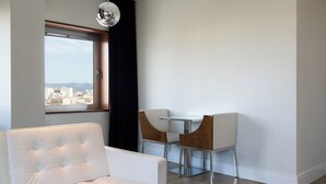 Ein modernes Wohnzimmer mit einem weißen Sofa, einem Esstisch mit zwei Stühlen und einem großen Fenster mit Blick auf die Stadt.